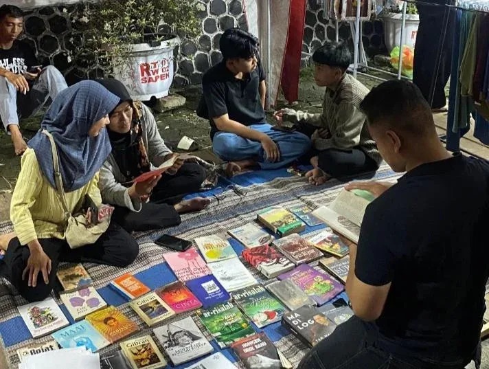 Pengunjung membaca buku di lapak komunitas literasi Boja sambil menikmati pertunjukan musik dalam acara Riuh Raya Boja di Jalan Veteran.