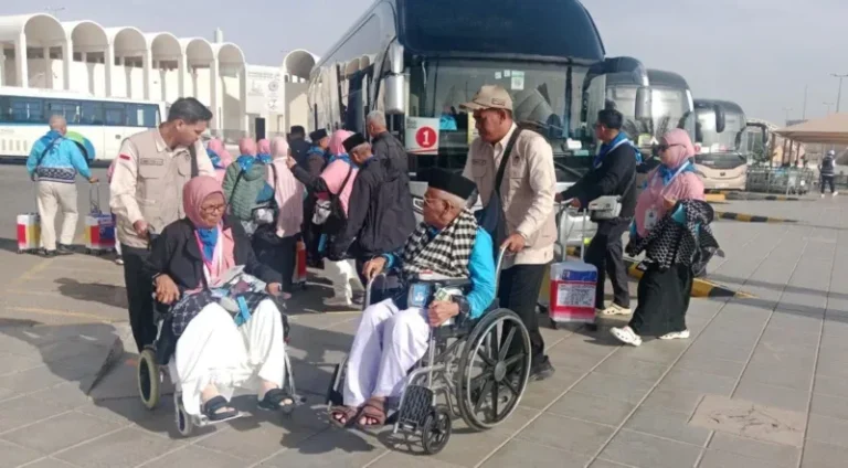 Petugas PPIH Arab Saudi Daker Bandara membantu dan mendorong jemaah haji lansia menggunakan kursi roda menuju bus untuk diberangkatkan ke hotel di Madinah. (Ahsan Fauzi/MCH 2026)